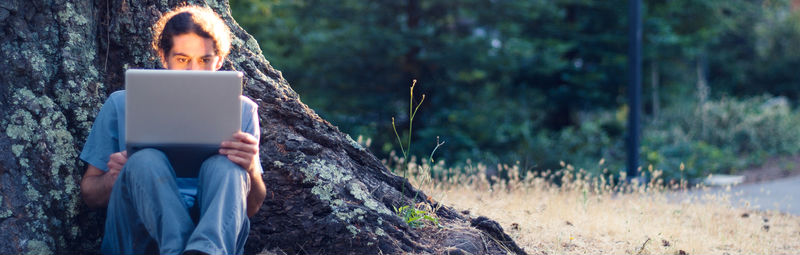 man with laptop leaning on tree